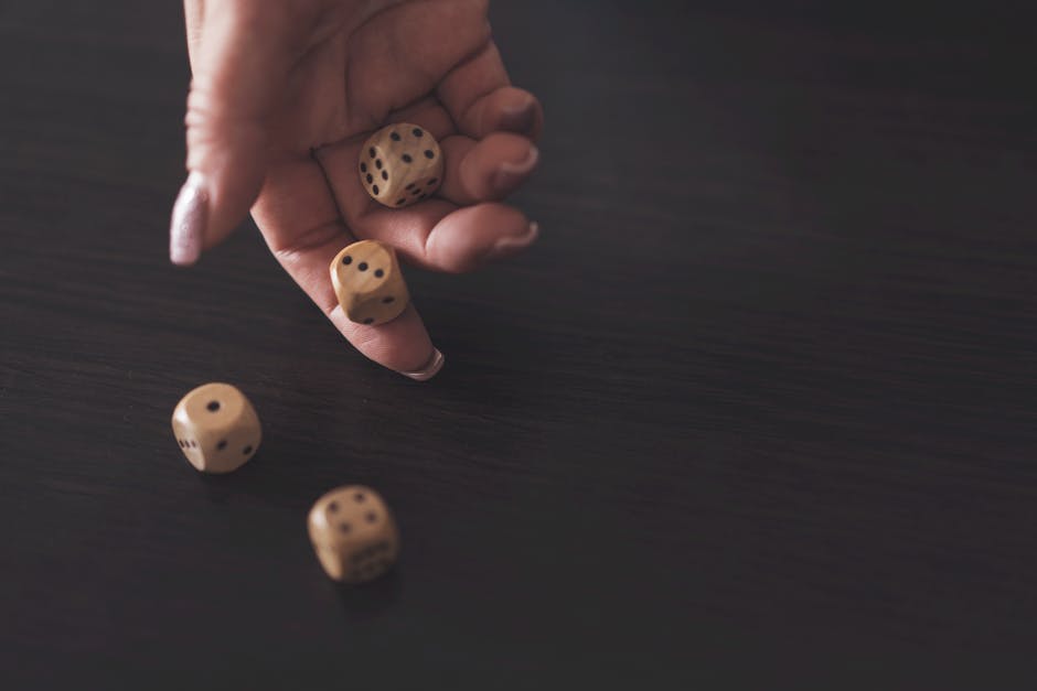 An image of a person rolling two dice towards a wooden box with multiple numbers on it, holding other dice in their hand waiting for their turn in playing the game Shut the Box. The game consists of multiple tiles and one player rolls the dice aiming to turn the tiles based on the numbers shown on the dice.