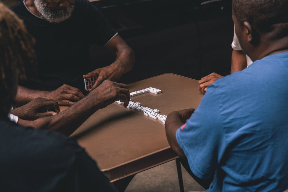 A picture of a few people gathered around a table playing the game of Mexican Train Dominoes, with tiles laid out in front of them.